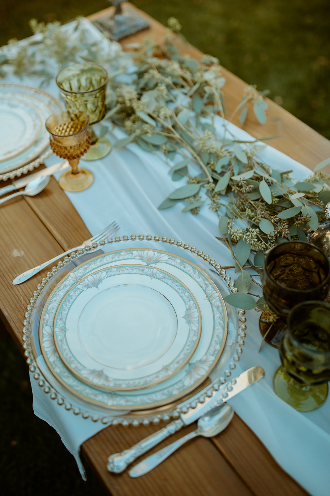 A reception table set with pearl rimmed plates, amber goblets and eucalyptus