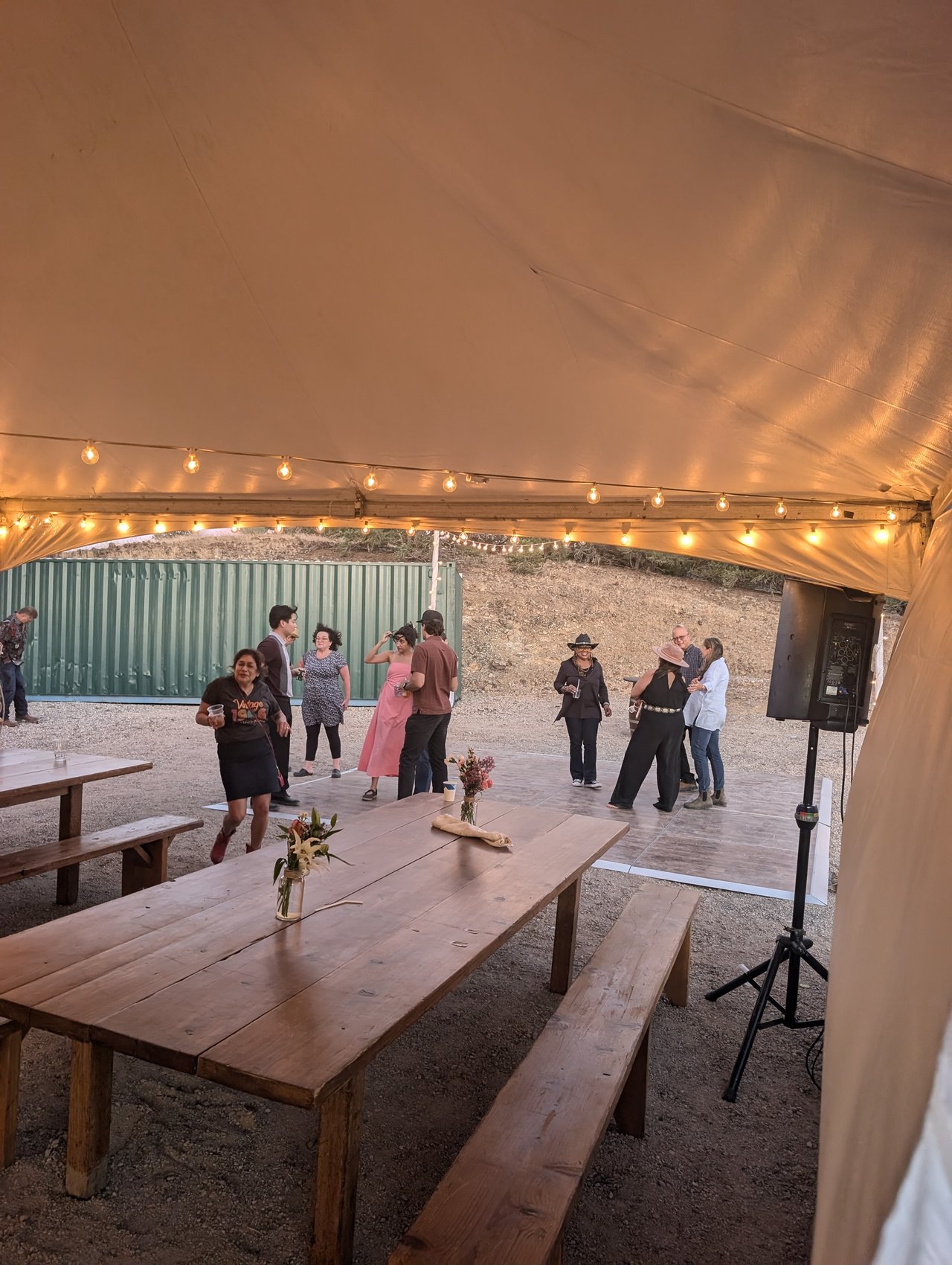 Guests dancing by the speaker at the open end of the tent under the string lights