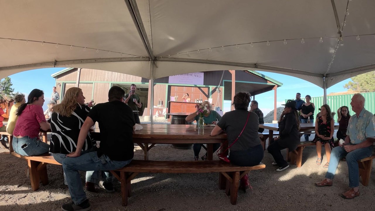 Guests at the long tables under the tent listening to a toast on the mic