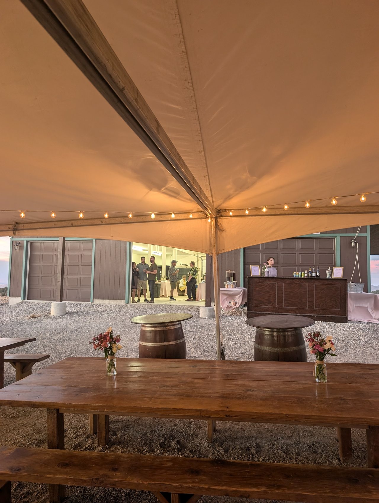 The bar under the tent with barrels, flowers and string lights
