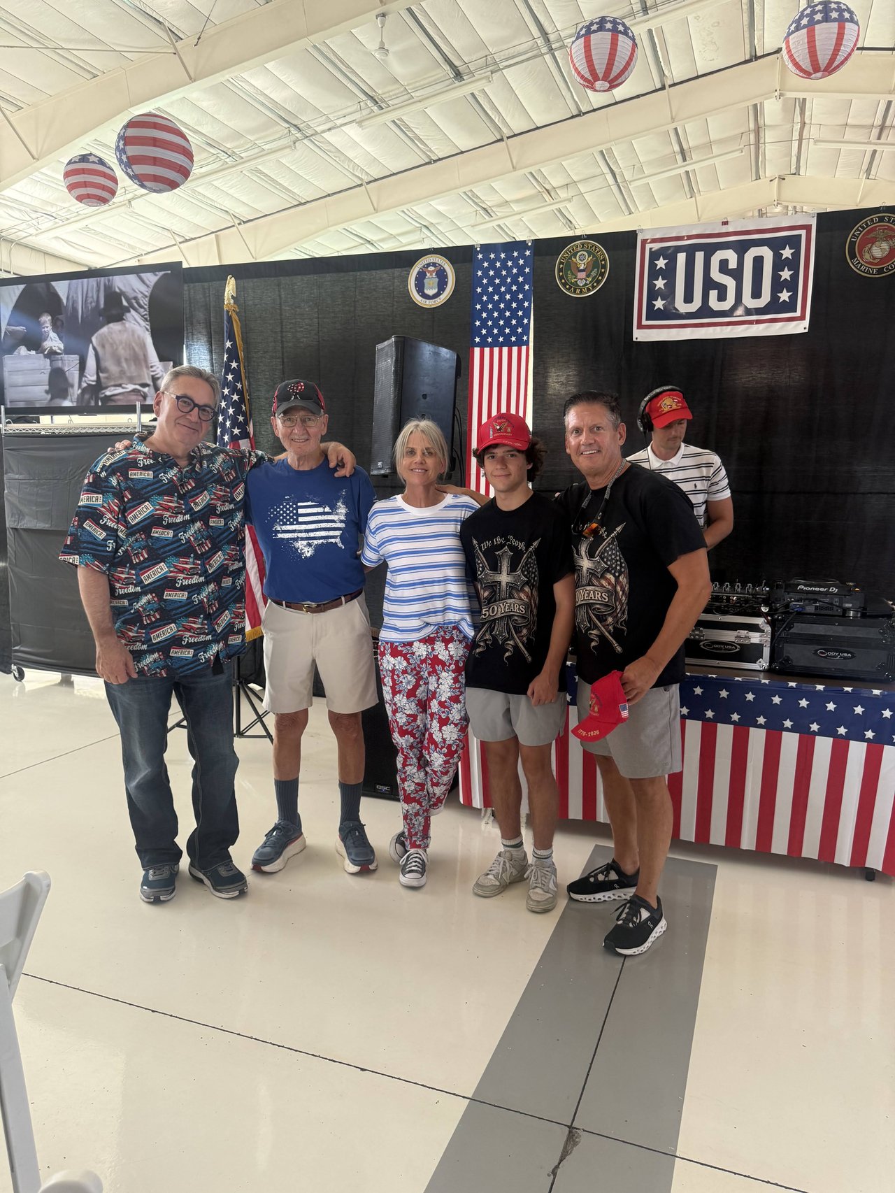 Five guests in flag shirts and red hats posing at the USO DJ booth