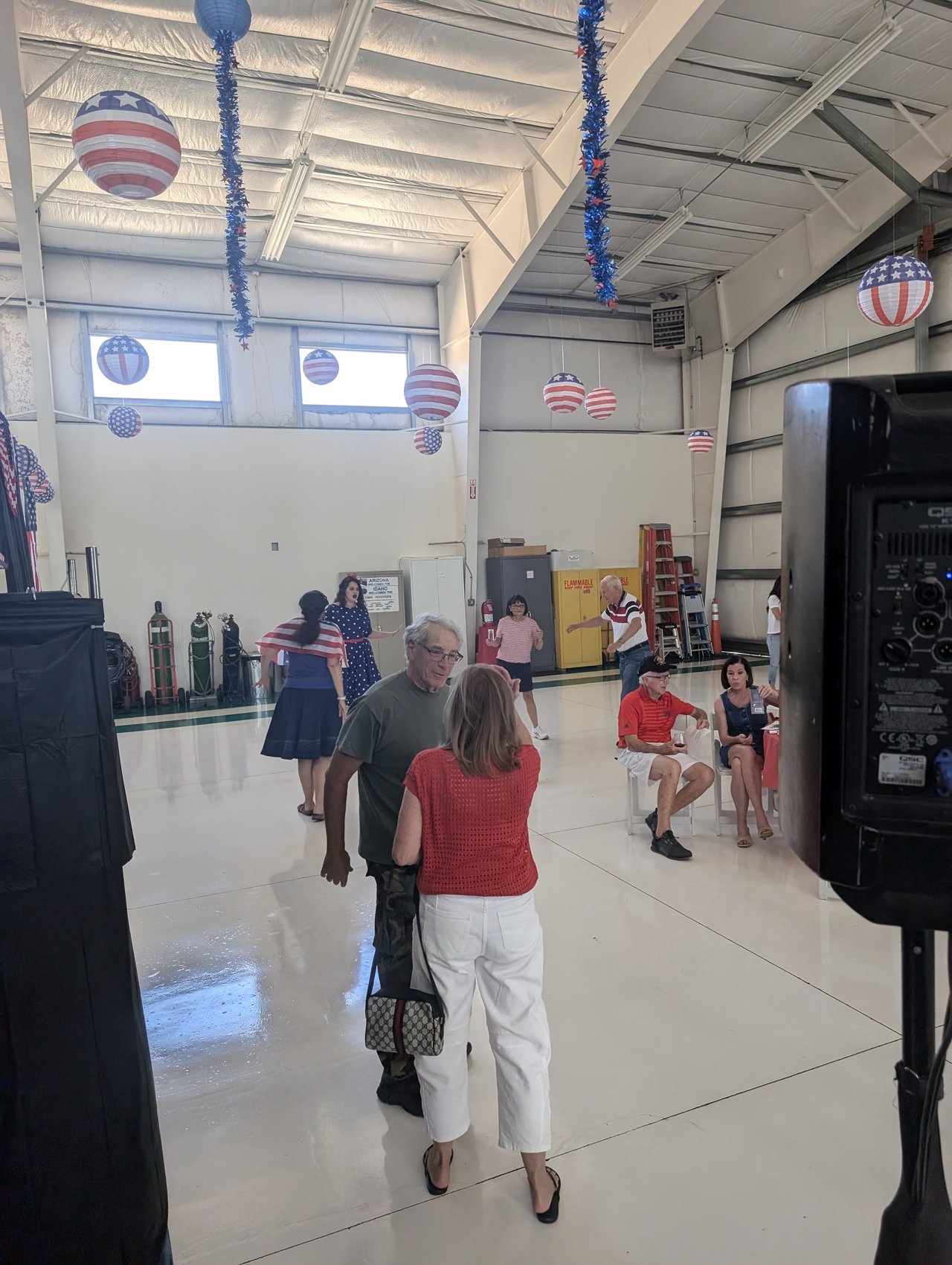 Guests in red and white chatting across the hangar floor beside the speaker