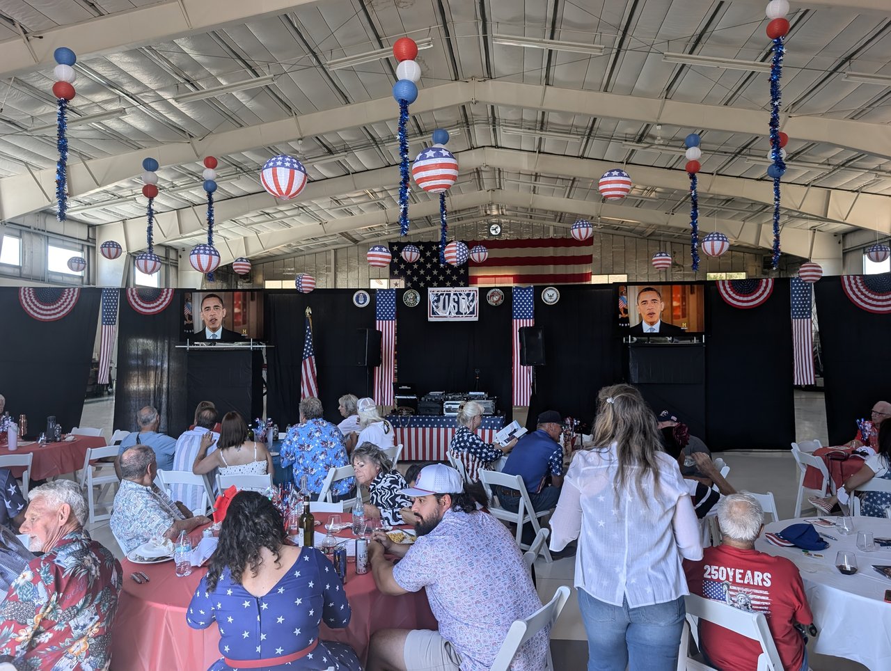 Guests at their tables watching the film on the screens by the USO stage
