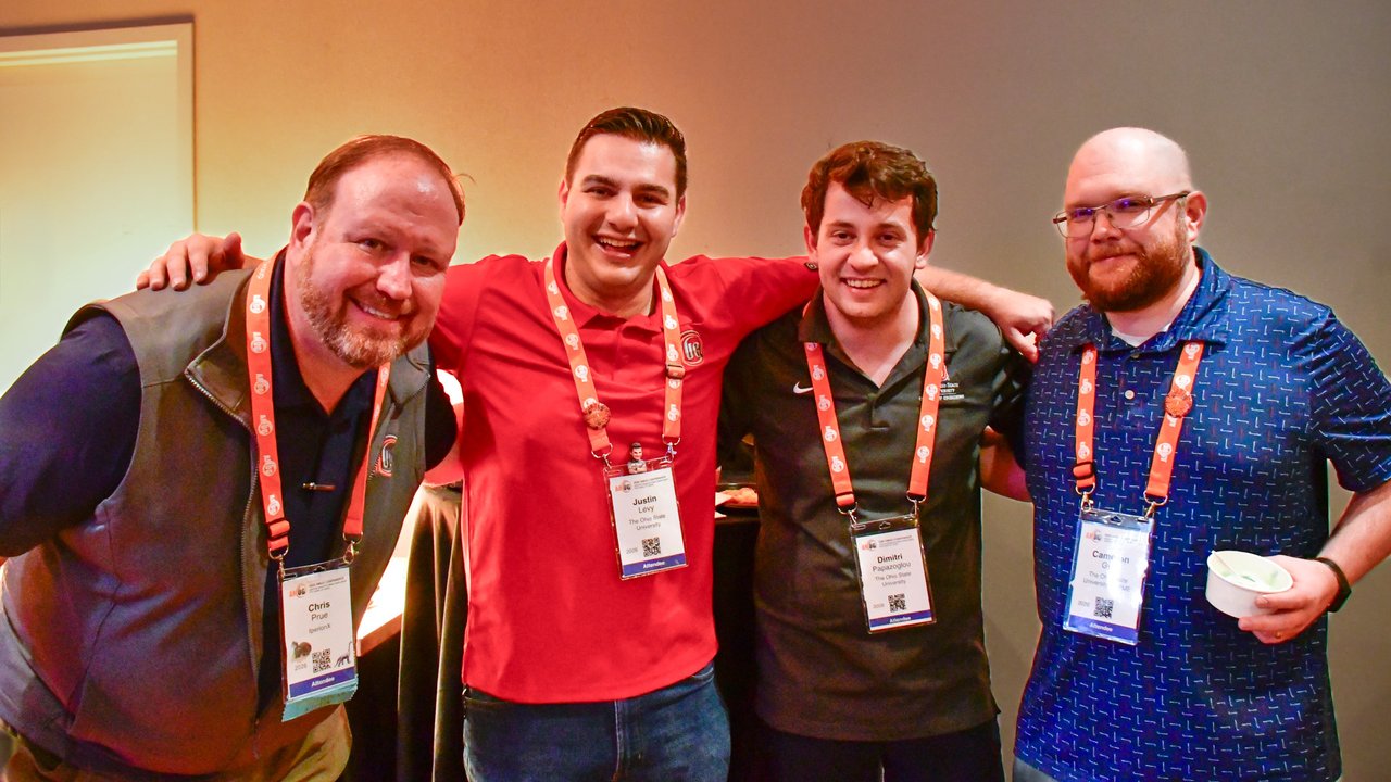 Four AMUG guests with lanyards smiling arm in arm