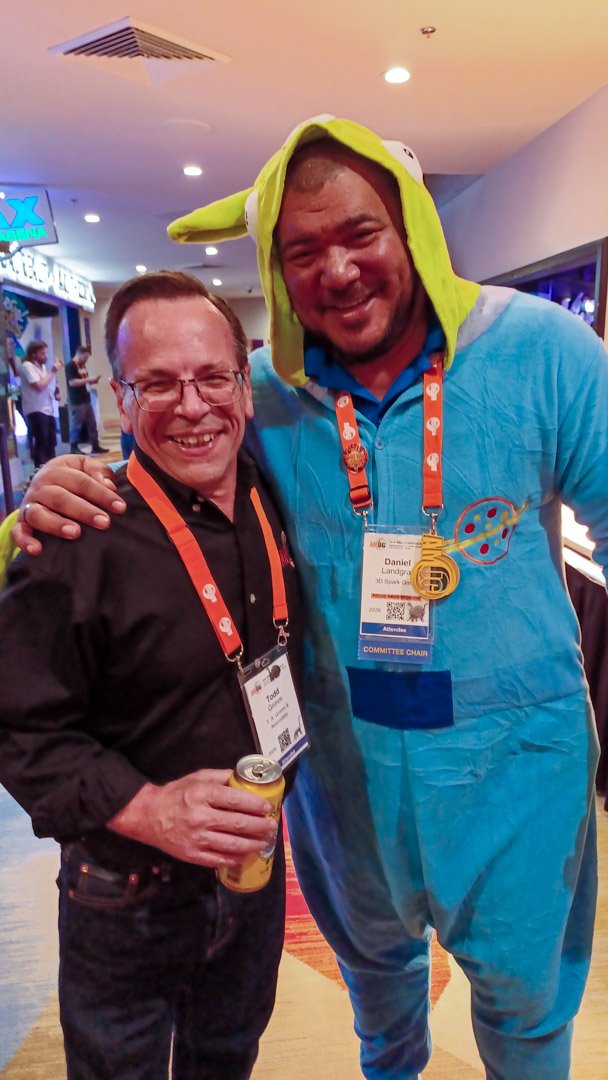 Two friends with lanyards, one in a blue dinosaur onesie, smiling together
