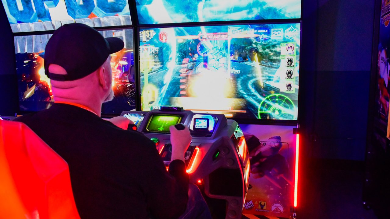 An AMUG guest playing a racing arcade game on a big screen