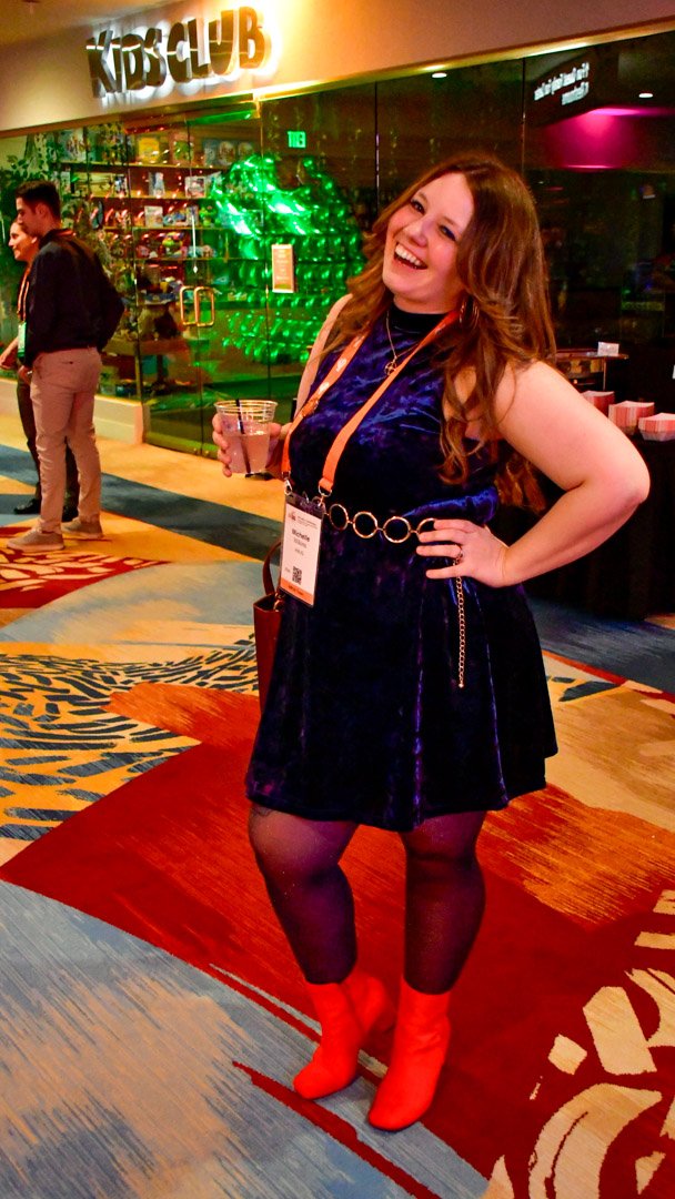 An AMUG guest in a blue velvet dress and red boots posing with a smile