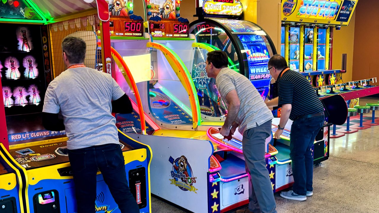 Three AMUG guests playing side by side arcade toss games