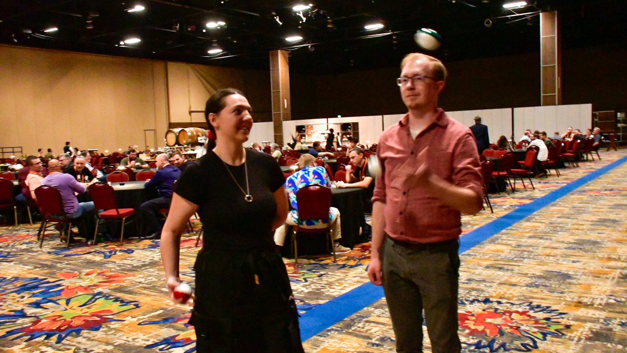 Two AMUG guests tossing a ball in the ballroom, full tables behind them