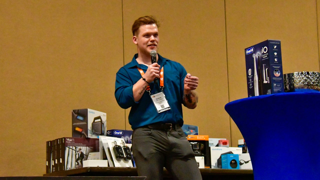 The host calling raffle prizes on the mic beside a table of prizes