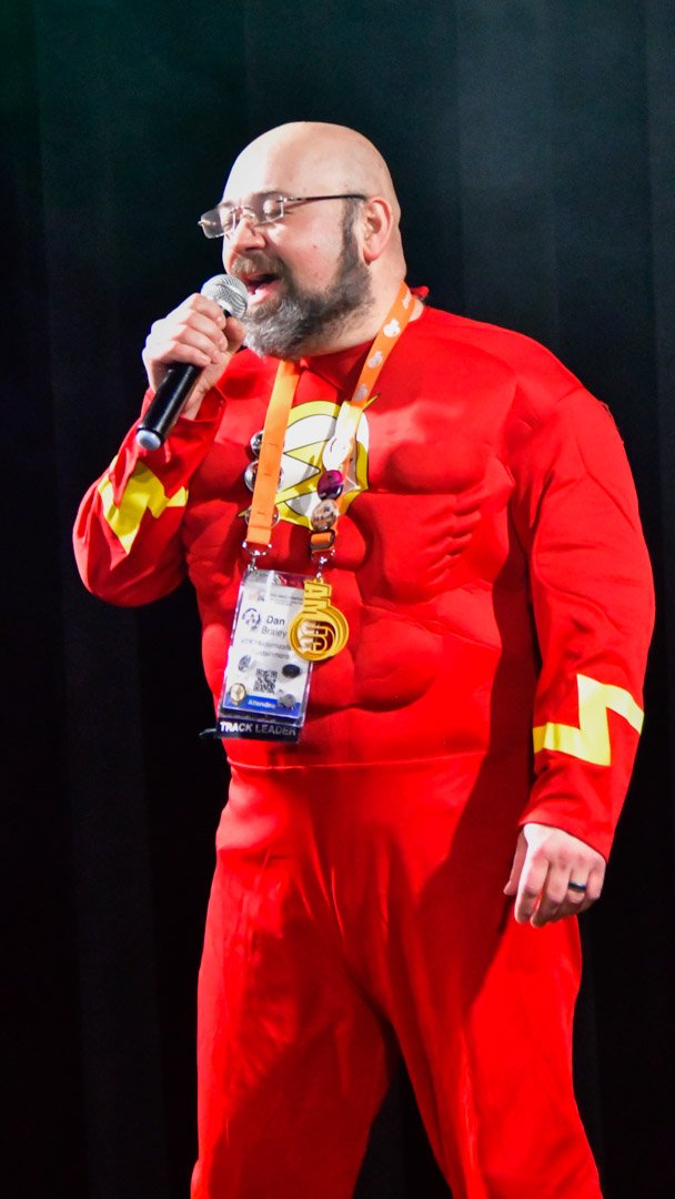An AMUG guest in a red superhero suit singing into the karaoke microphone
