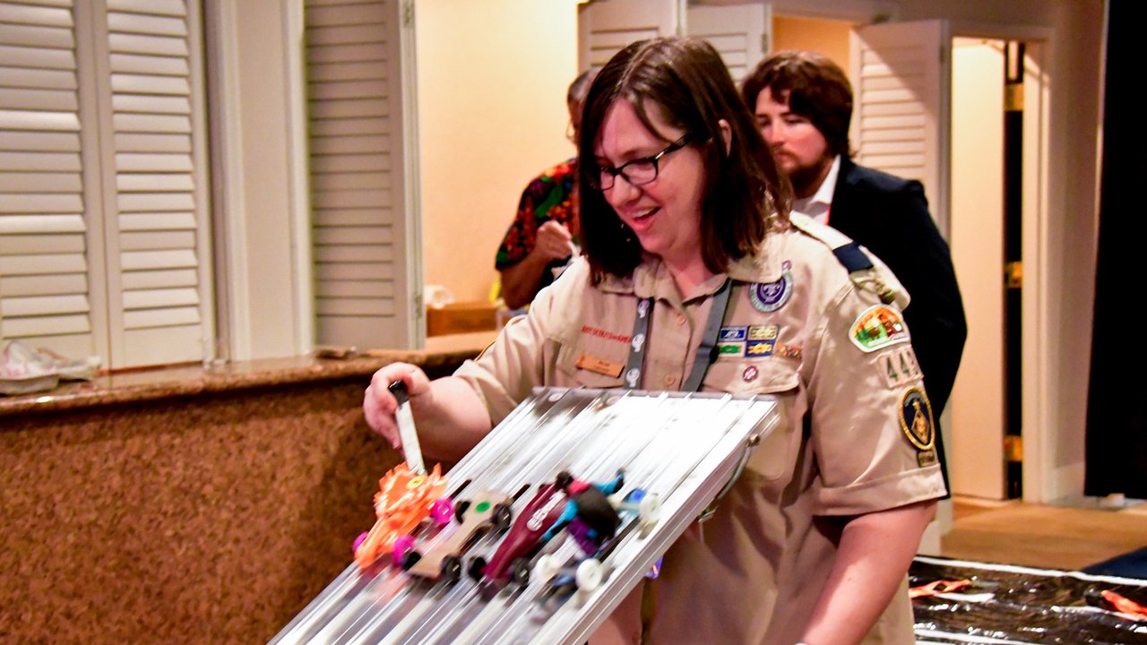 A guest in a scout uniform lining up derby cars at the top of the track