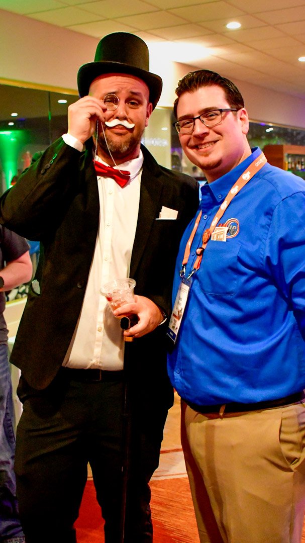 An AMUG guest dressed as the Monopoly man in a top hat beside a smiling friend