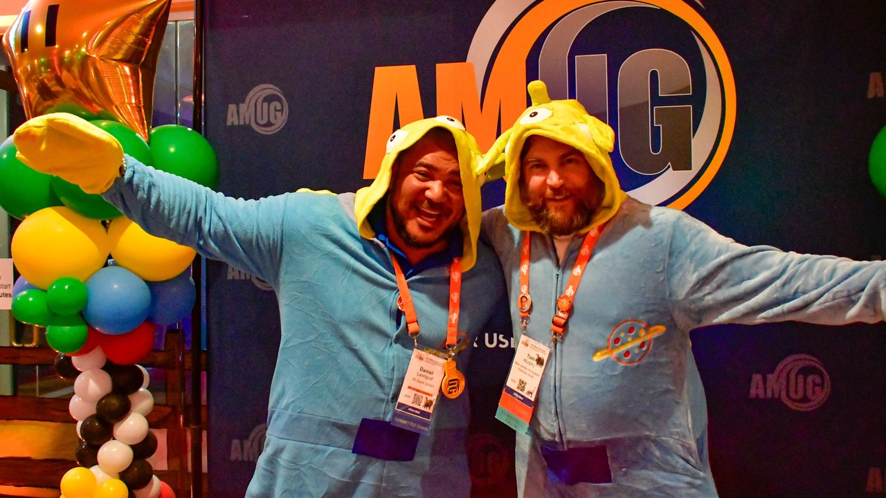Two AMUG guests in blue onesies with arms out in front of the AMUG sign