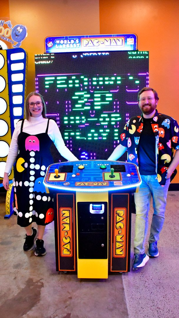 Two AMUG guests in Pac Man outfits posing by a giant Pac Man arcade game