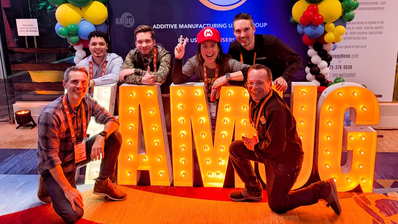 A team of AMUG guests posing behind the lighted AMUG letters, one in a Mario hat
