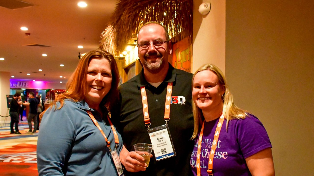 Three smiling AMUG guests with lanyards and drinks