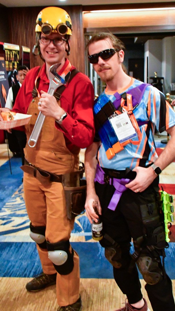 Two AMUG guests in game character costumes, one holding a big wrench