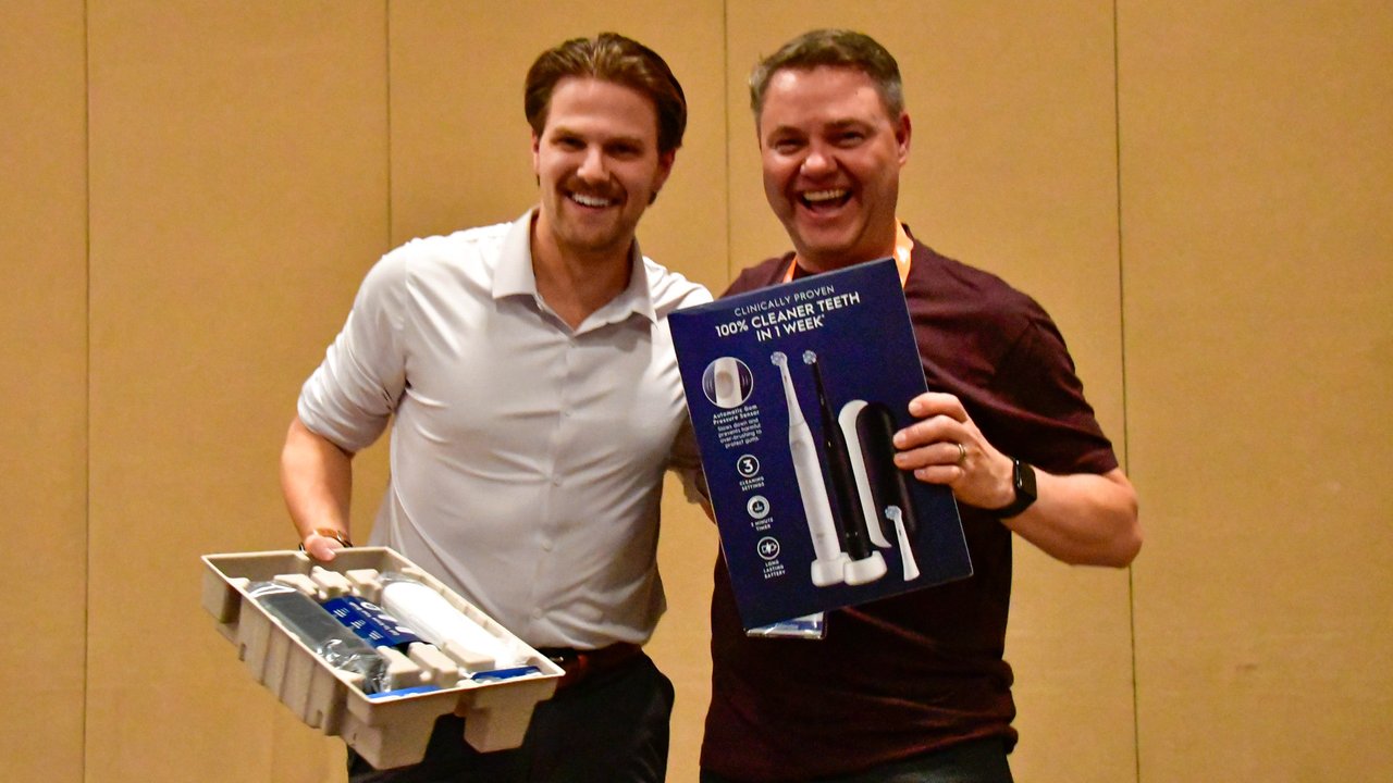 Two AMUG guests laughing with the toothbrush set they won