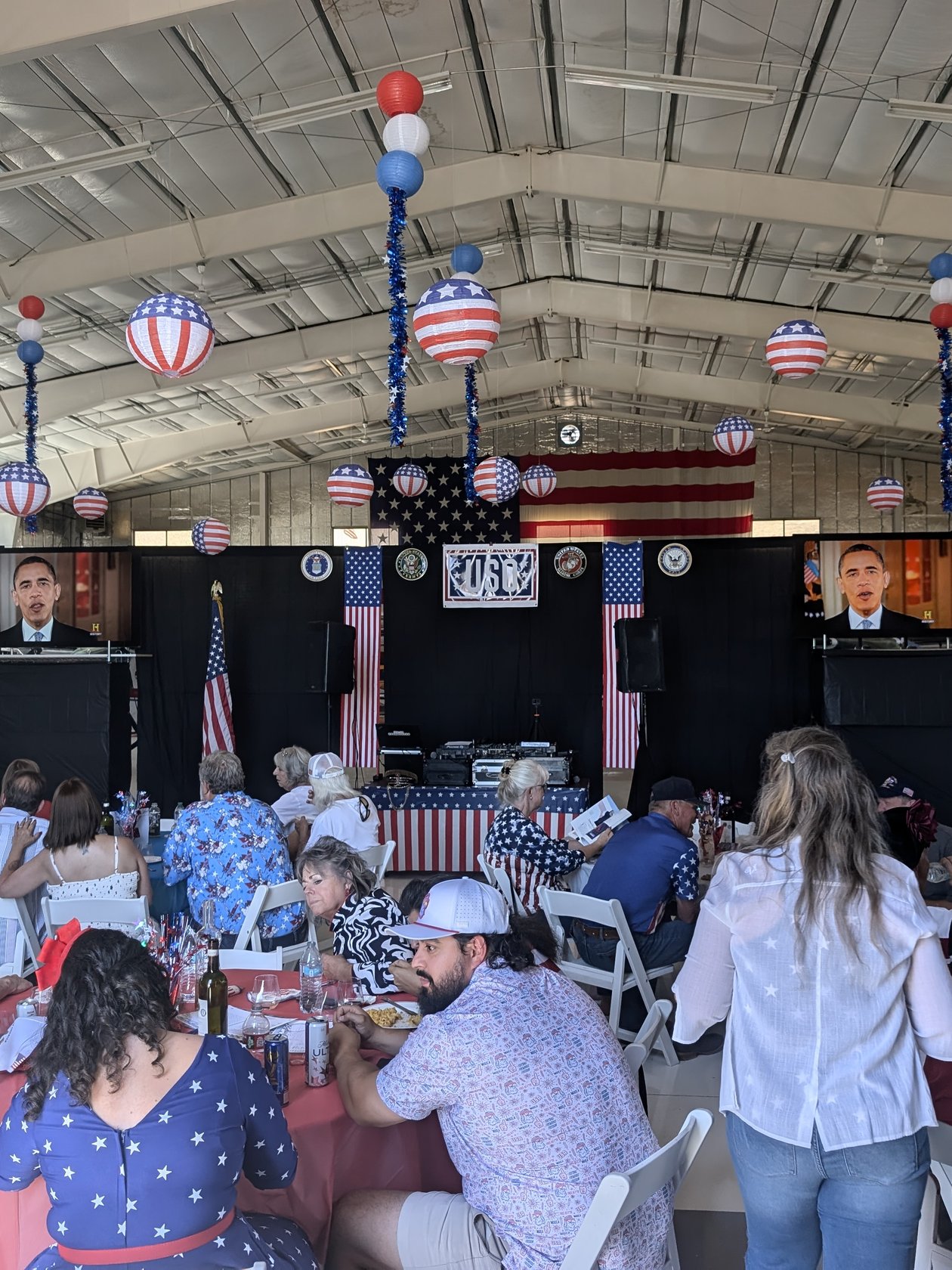 Guests at their tables facing the USO stage and screens in a hangar hung with flags and star spangled lanterns