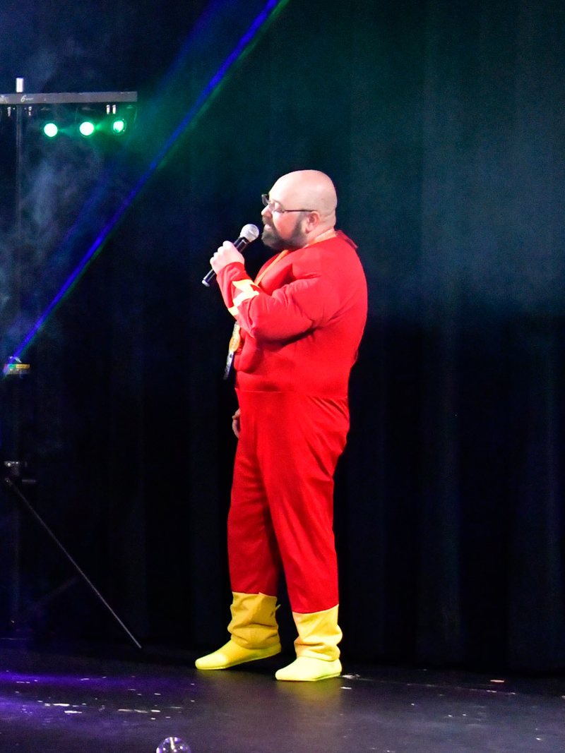 An AMUG guest in a red superhero suit singing karaoke under green lasers and fog