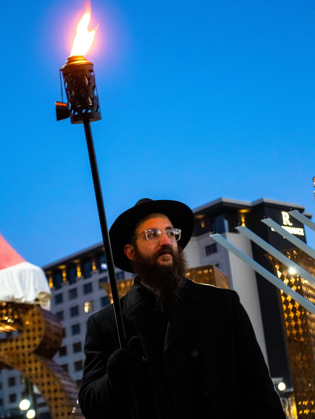 Rabbi Mendel Cunin holding the torch beside the City Plaza menorah at dusk