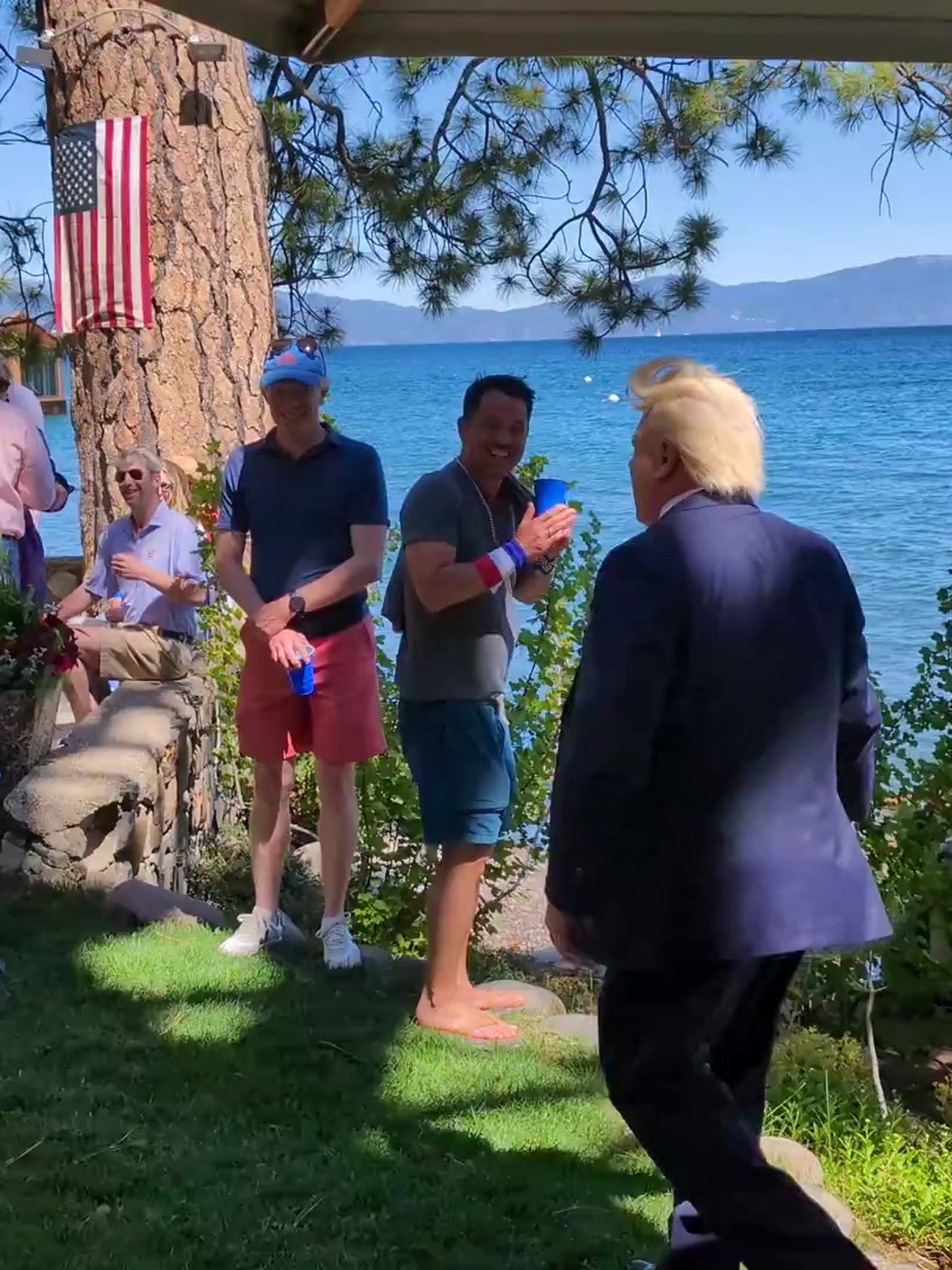 A Trump impersonator greets guests by the American flag on the pine, with Lake Tahoe behind them