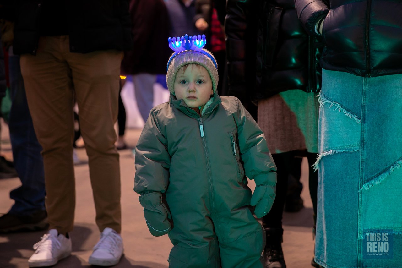A child in a green snowsuit wears a light up menorah headband