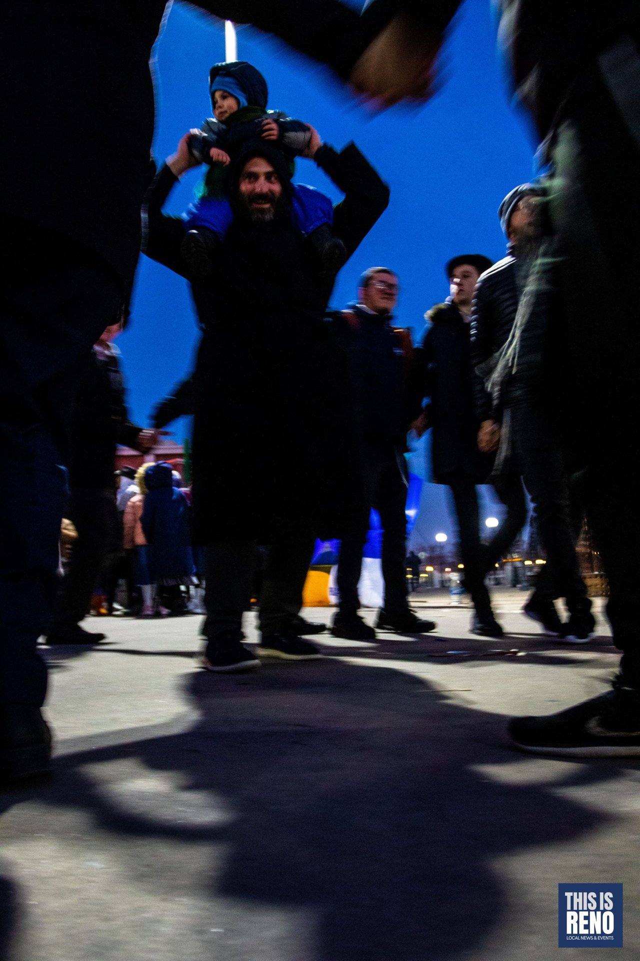A child rides on a father's shoulders in the evening crowd