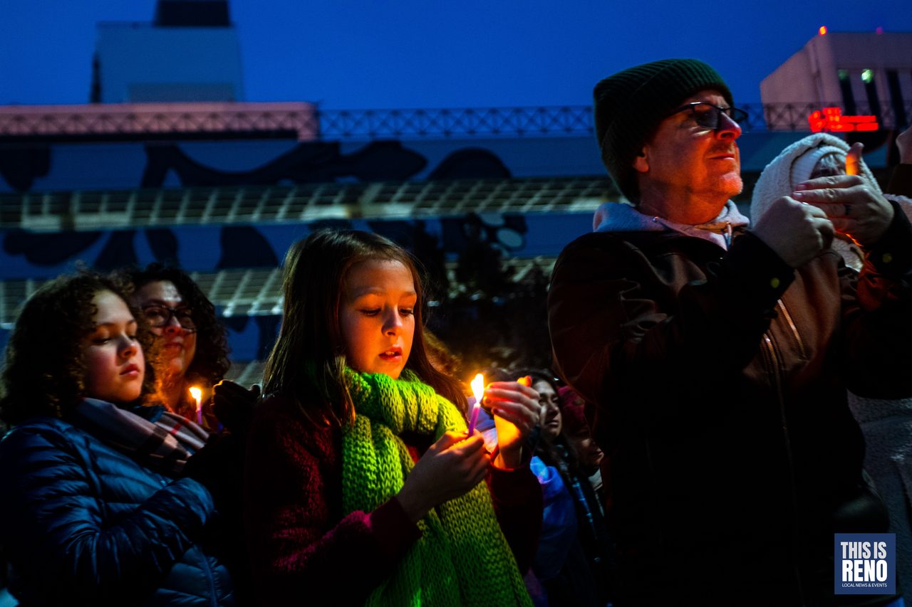 Families holding candles in front of the downtown lights