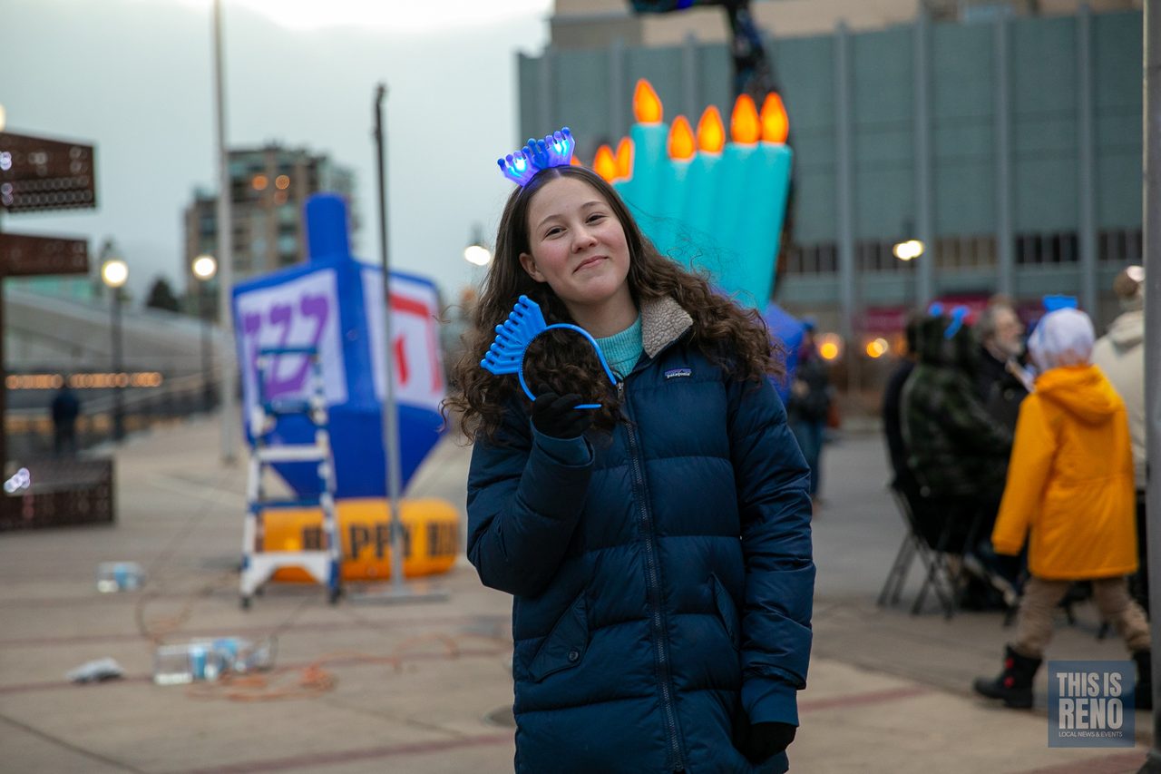 A girl in a menorah headband waving by the giant dreidel