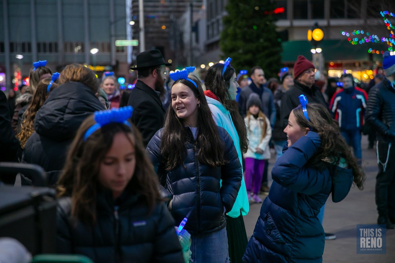 Girls laugh together in light up menorah headbands in the crowd