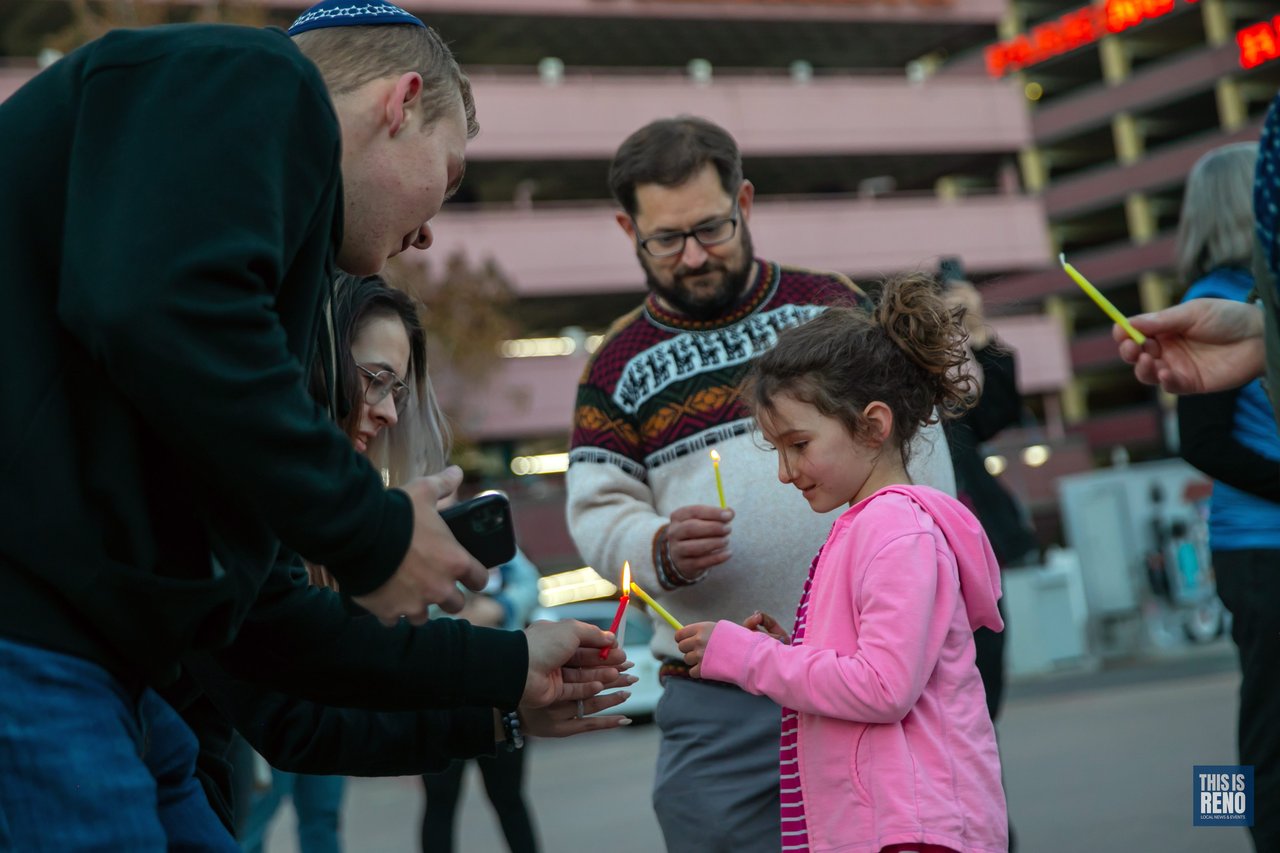 A man lights a girl’s candle in the crowd before the menorah is lit