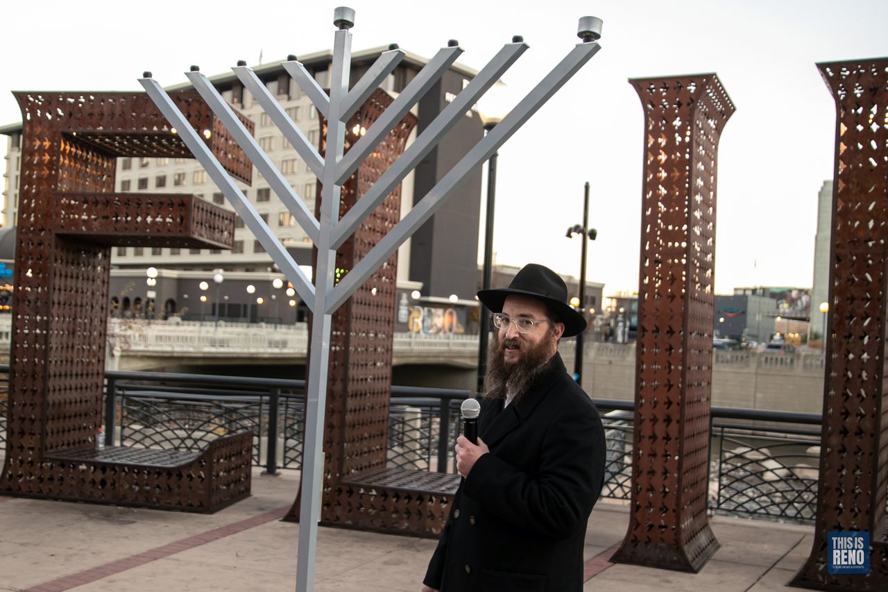 A rabbi with a microphone beside the menorah and the Believe sign