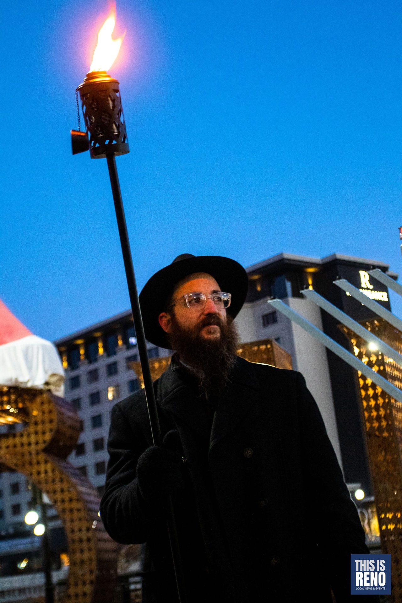 A rabbi holds the lit torch against the blue evening sky