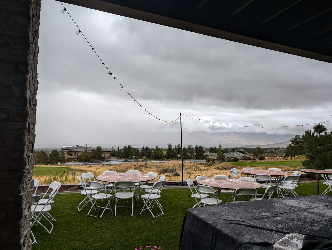 String lights over the round tables on the lawn under a cloudy afternoon sky