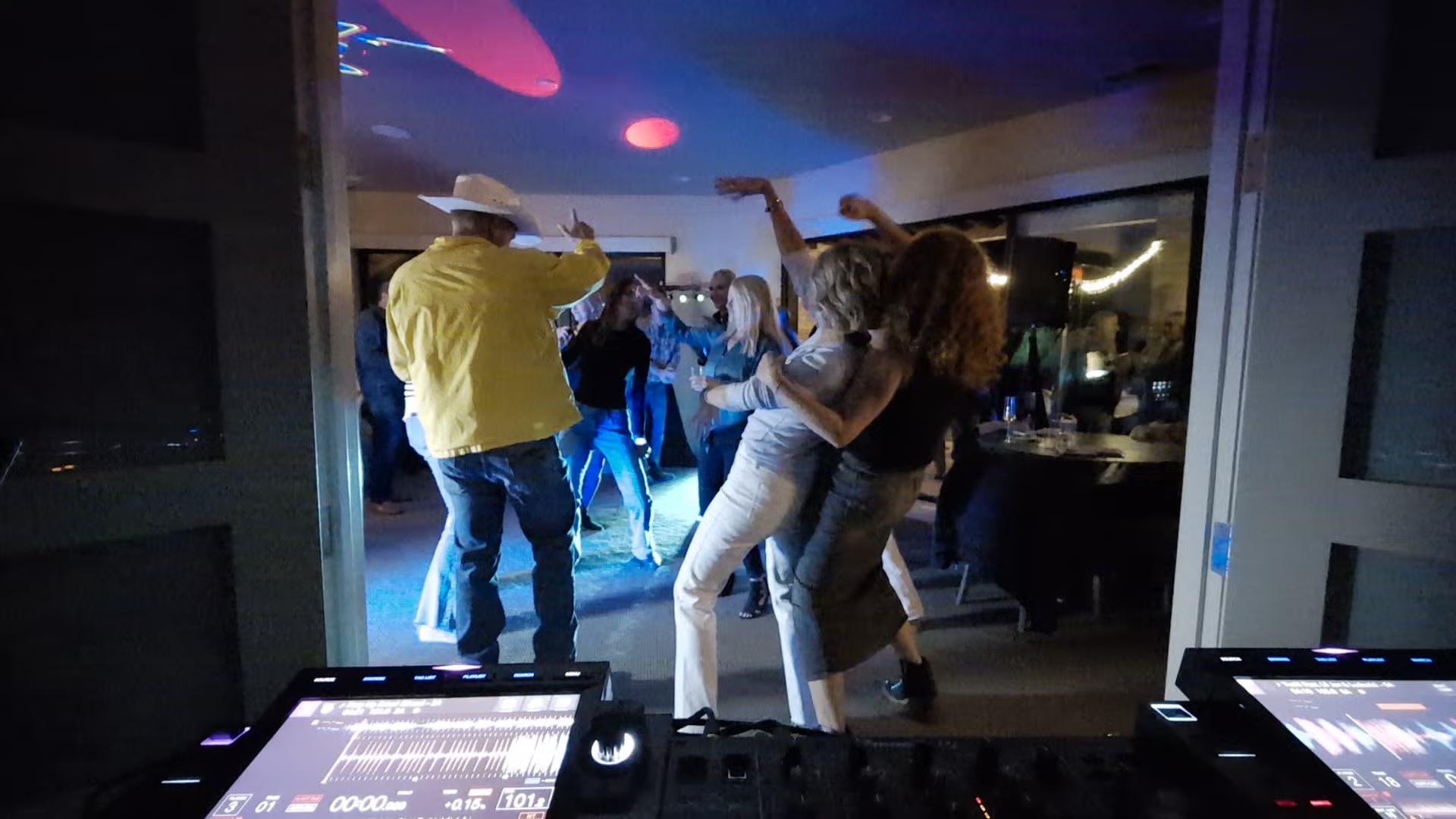 A guest in a cowboy hat and yellow jacket dancing in the living room, seen from behind the DJ booth at John’s 50th birthday in ArrowCreek