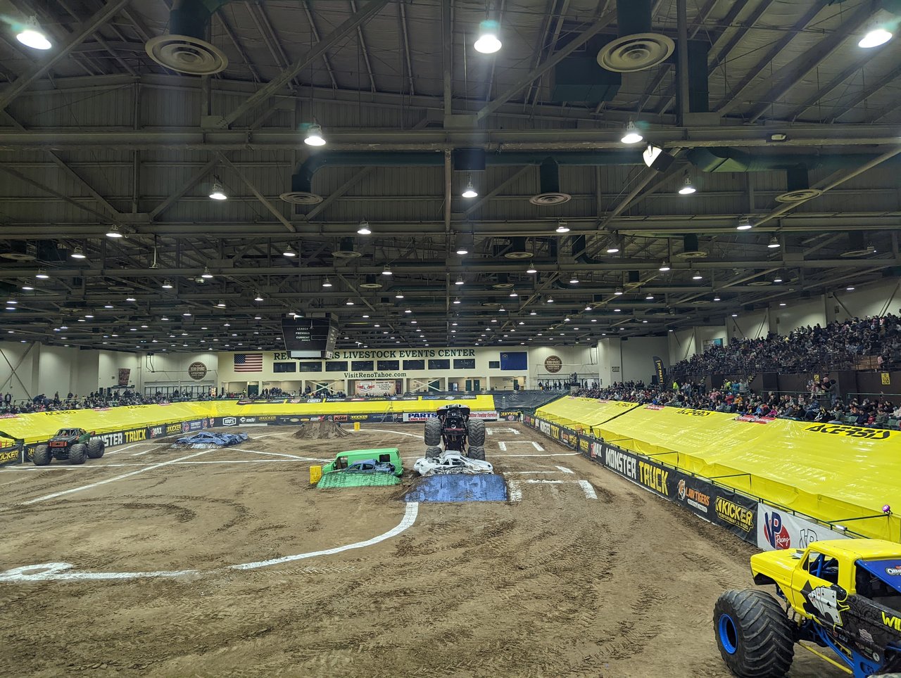 Monster trucks lined up on the track under the arena lights with full stands behind them