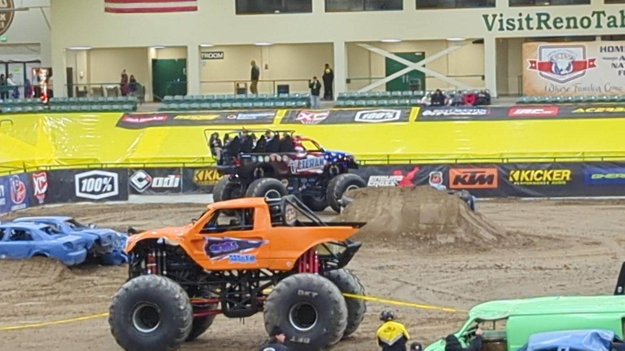 An orange monster truck climbing onto the crushed cars