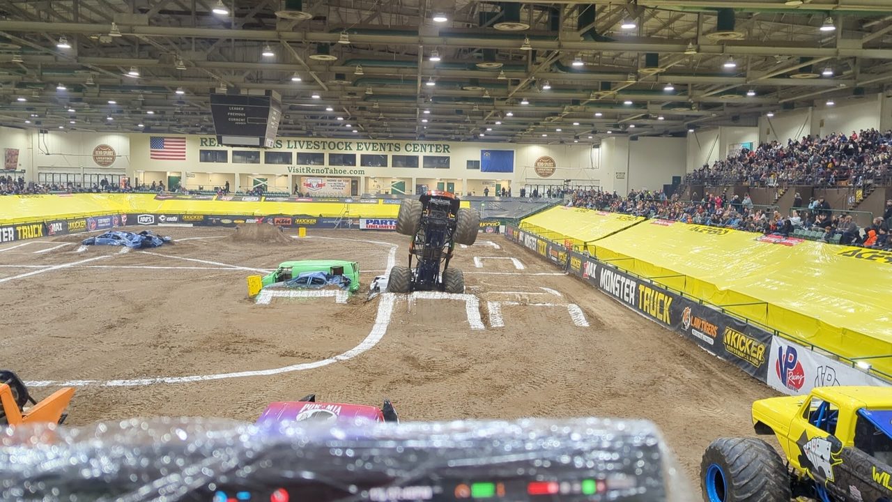 A monster truck standing up on its back wheels in front of the packed stands, seen from my booth