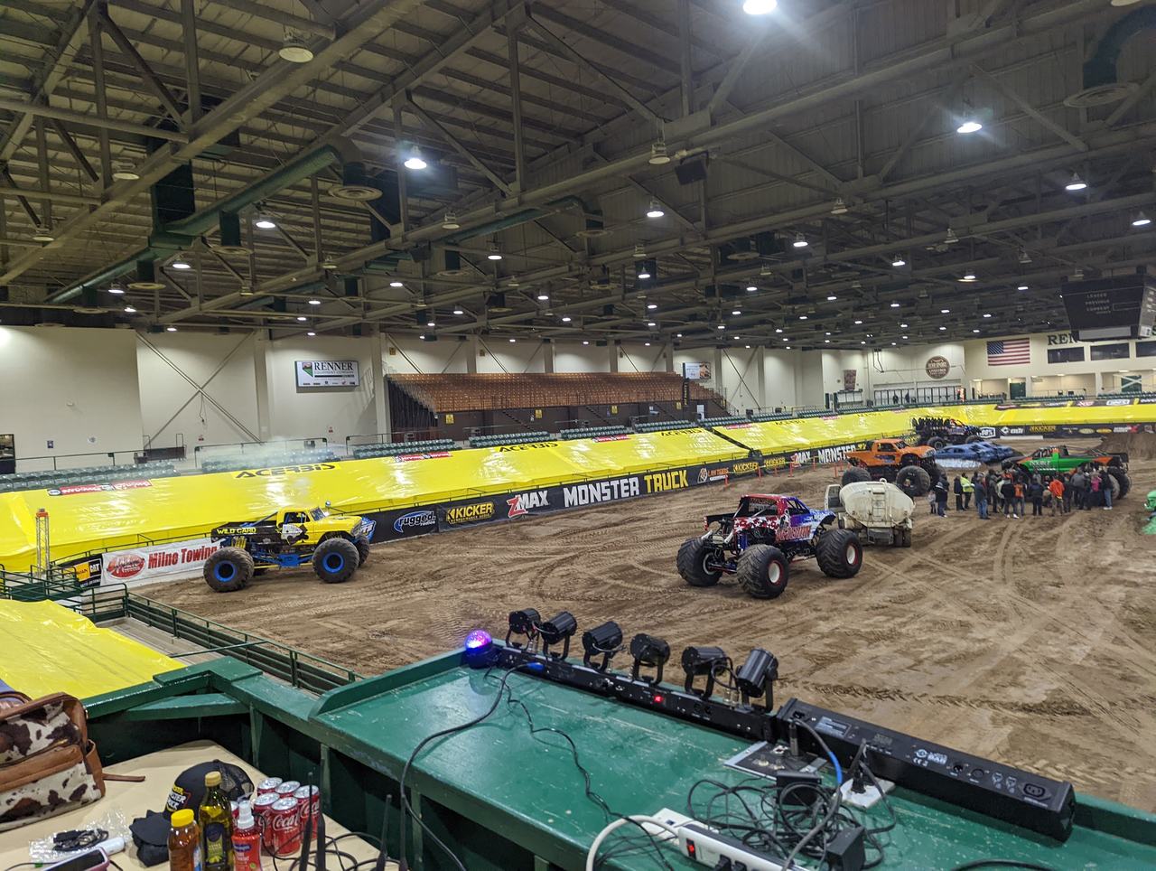 Monster trucks lined up on the track, seen from the DJ booth lights at the rail