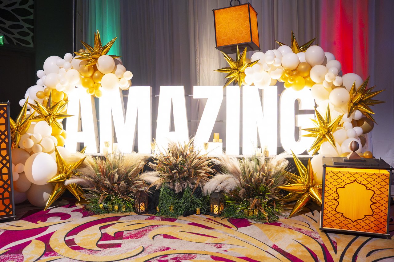 The Amazing letters under the gold and white balloon arch