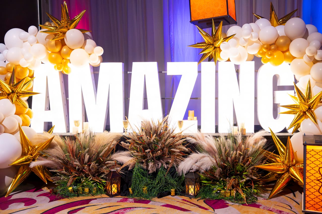 The lit AMAZING letters framed by white balloons, gold stars and pampas grass