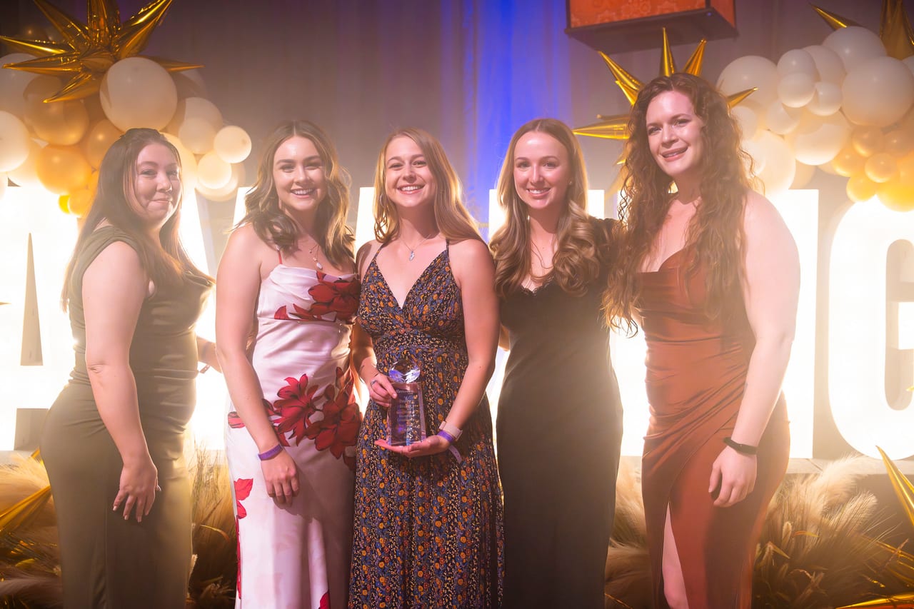Five Renown teammates at the lit letters, one holding her award