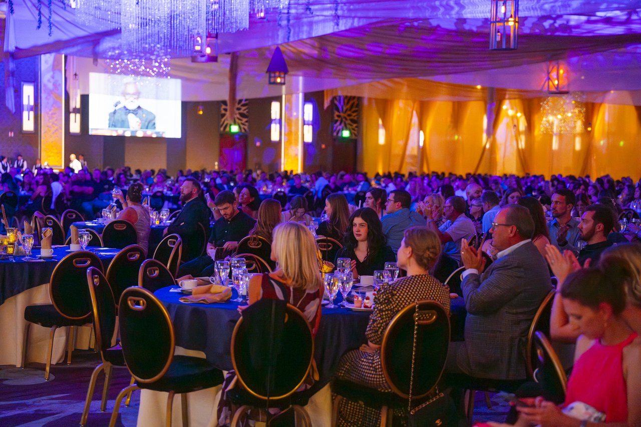The packed ballroom cheering a speaker on the screen