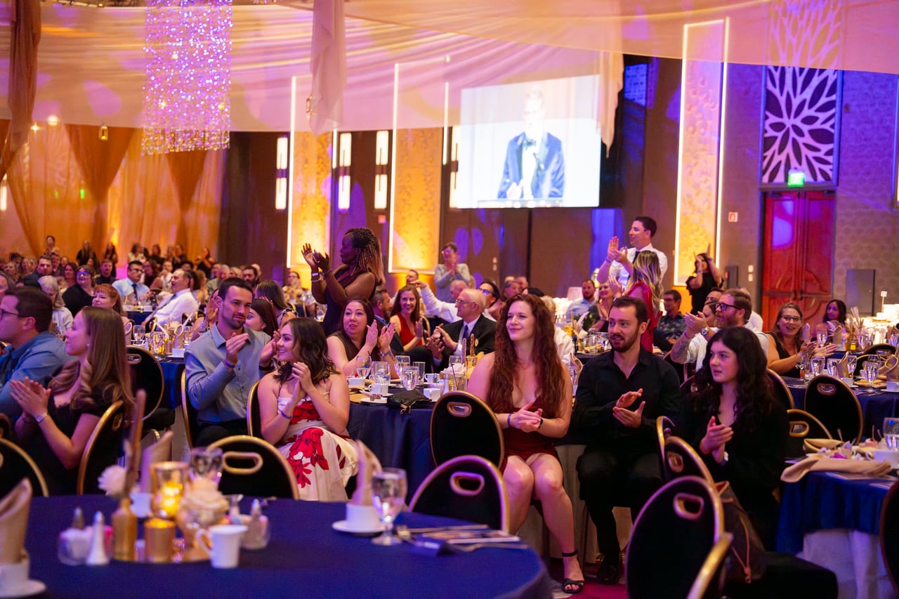 A ballroom of Renown guests cheering as a speaker takes the screen
