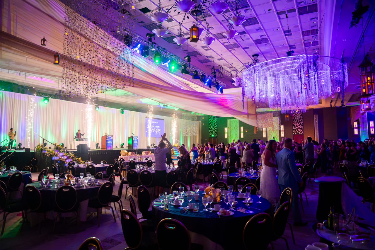 The Tuscany Ballroom from the back, set with blue tables, chandeliers and the stage lit up