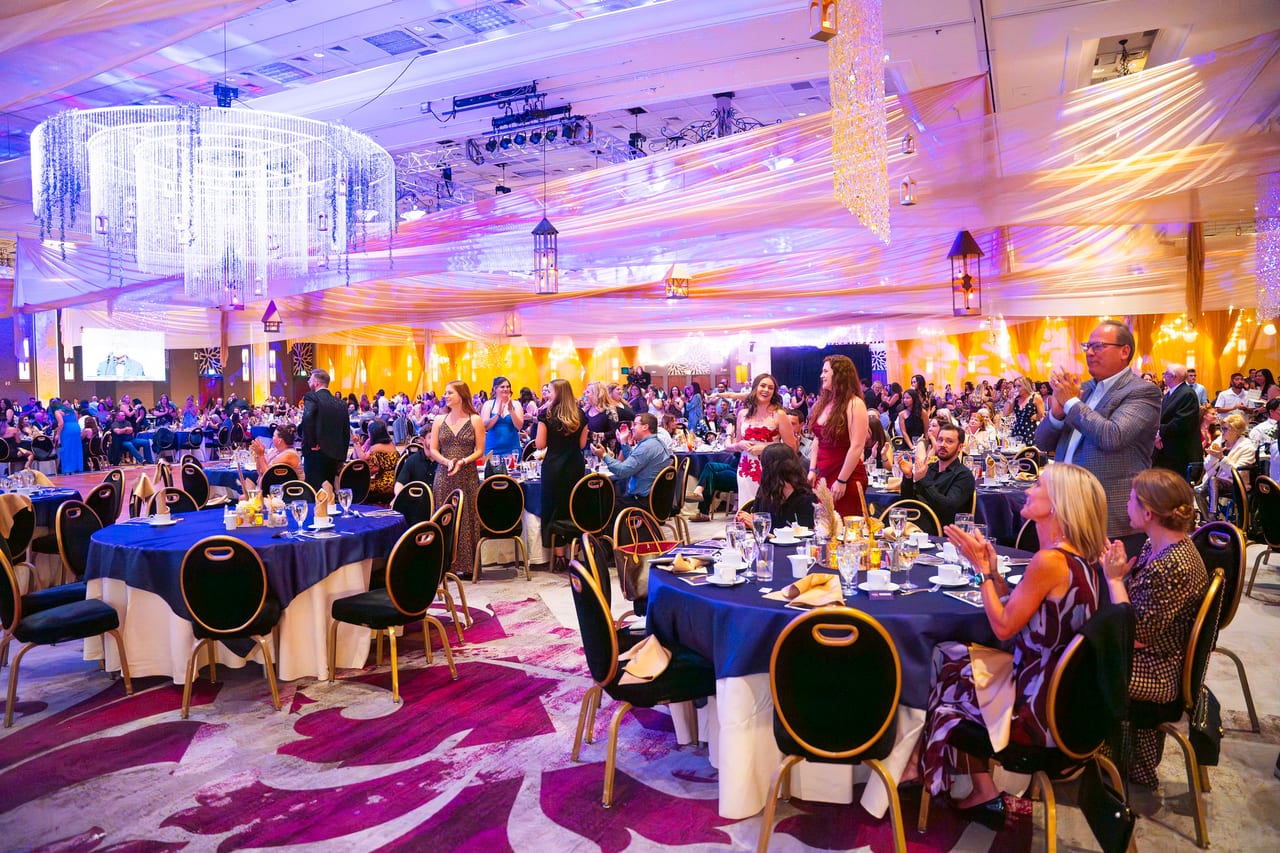 Renown guests rising from their tables to cheer across the ballroom
