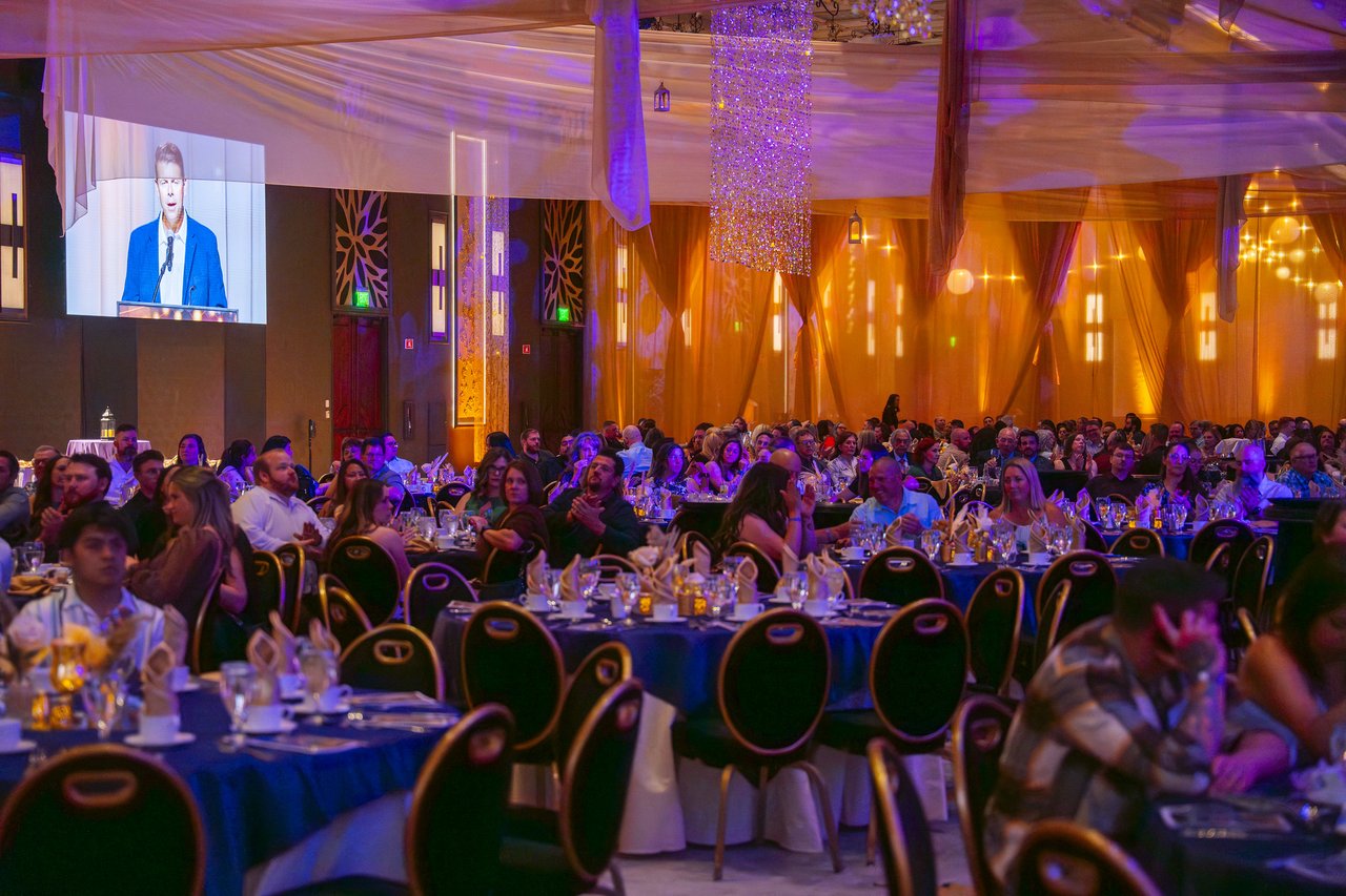 The ballroom tables under gold lights with a speaker on the screen
