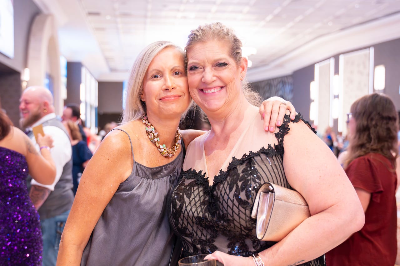 Two Renown friends cheek to cheek in the ballroom foyer